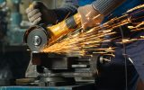 Locksmith in special clothes and goggles works in production. Metal processing with angle grinder. Sparks in metalworking.